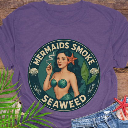 Purple t-shirt with mermaid graphic and 'Mermaids Smoke Seaweed' text on a wooden surface.