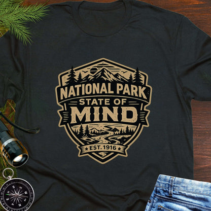 Black outdoor t-shirt flat lay with vintage badge graphic reading “National Park State of Mind” and “Est. 1916,” featuring mountains, trees, and a winding river.