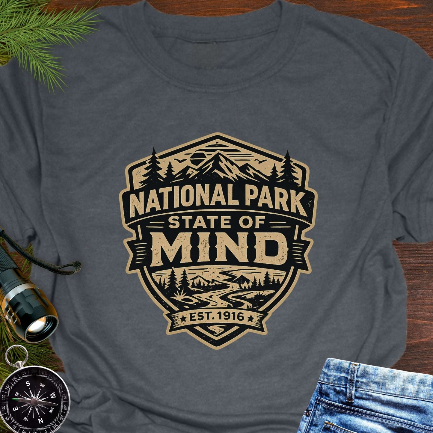 Dark Gray outdoor t-shirt flat lay with vintage badge graphic reading “National Park State of Mind” and “Est. 1916,” featuring mountains, trees, and a winding river.