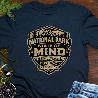 Navy blue outdoor t-shirt flat lay with vintage badge graphic reading “National Park State of Mind” and “Est. 1916,” featuring mountains, trees, and a winding river.