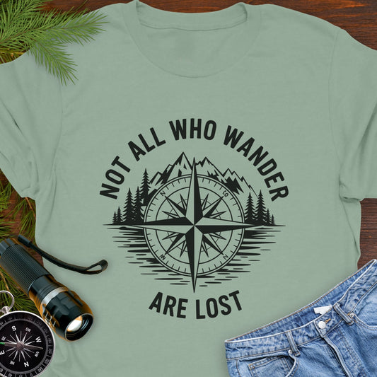 Sage T-shirt with a mountain range and lake with a compass overlay that says Not All Who Wander are Lost.
