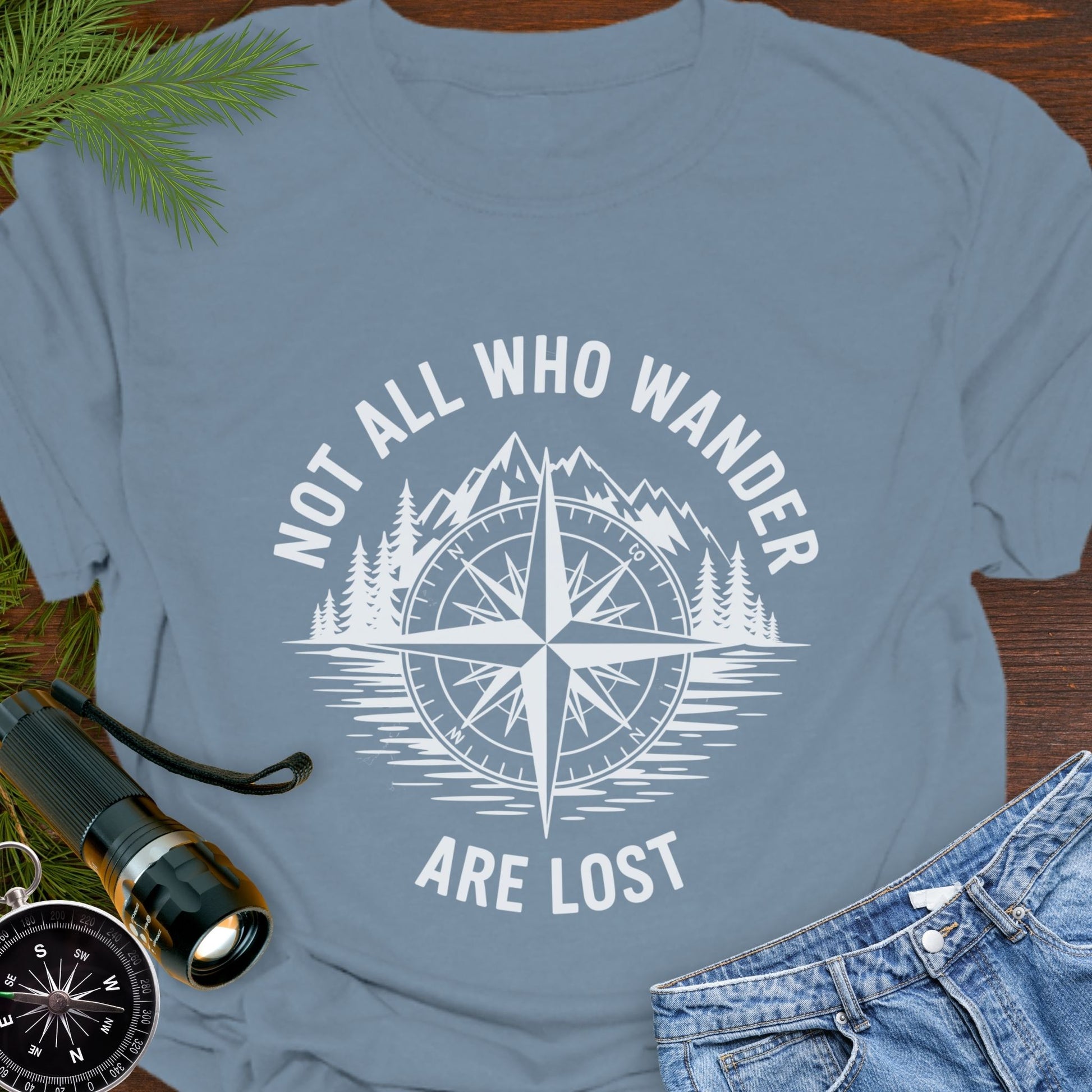 Stone Blue  T-shirt with a mountain range and lake with a compass overlay that says Not All Who Wander are Lost. 