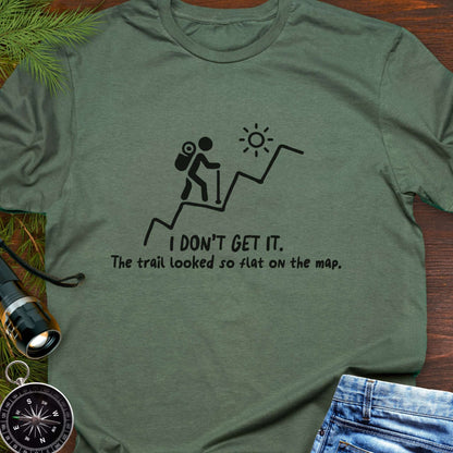 Green hiking t-shirt flat lay with white graphic of a backpacker climbing a steep trail and text: “I DON’T GET IT. The trail looked so flat on the map.”