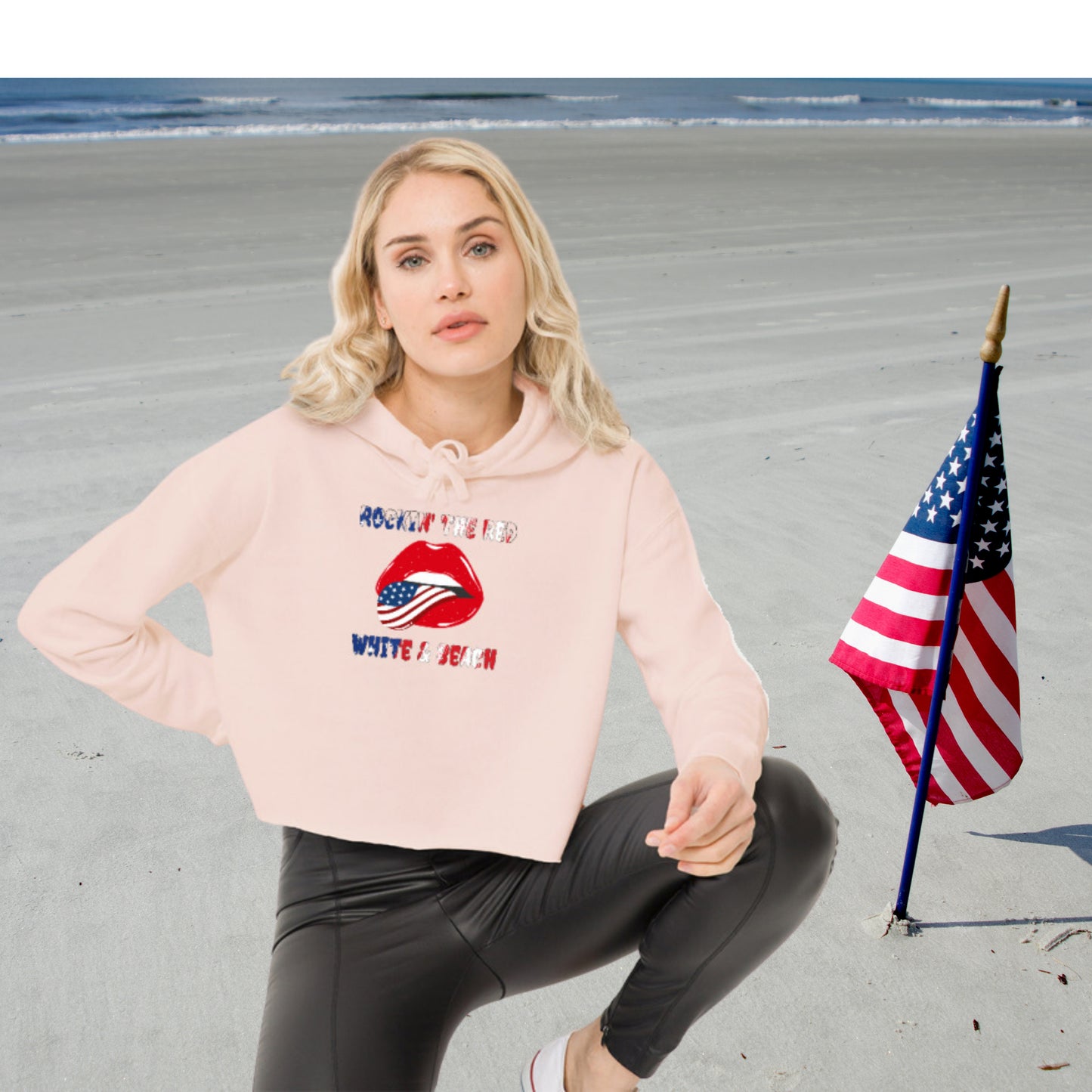 woman kneeling down on the beach in a light pink cropped hoodie with rolling stone lips with the american flag tongue with flag text that says Rockin' the Red White and Blue 