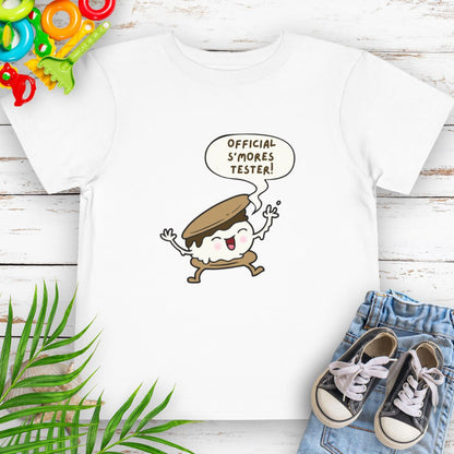 White Toddler T-shirt with "Official S'mores Tester" text in speech bubble over a S'more character – perfect for camping and summer fun.