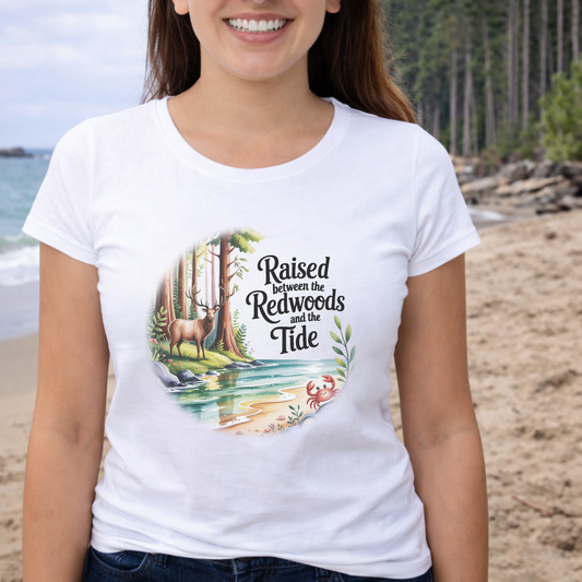 Person wearing a white t-shirt with nature-themed design with text Raised between the Redwoods and The Tide.
