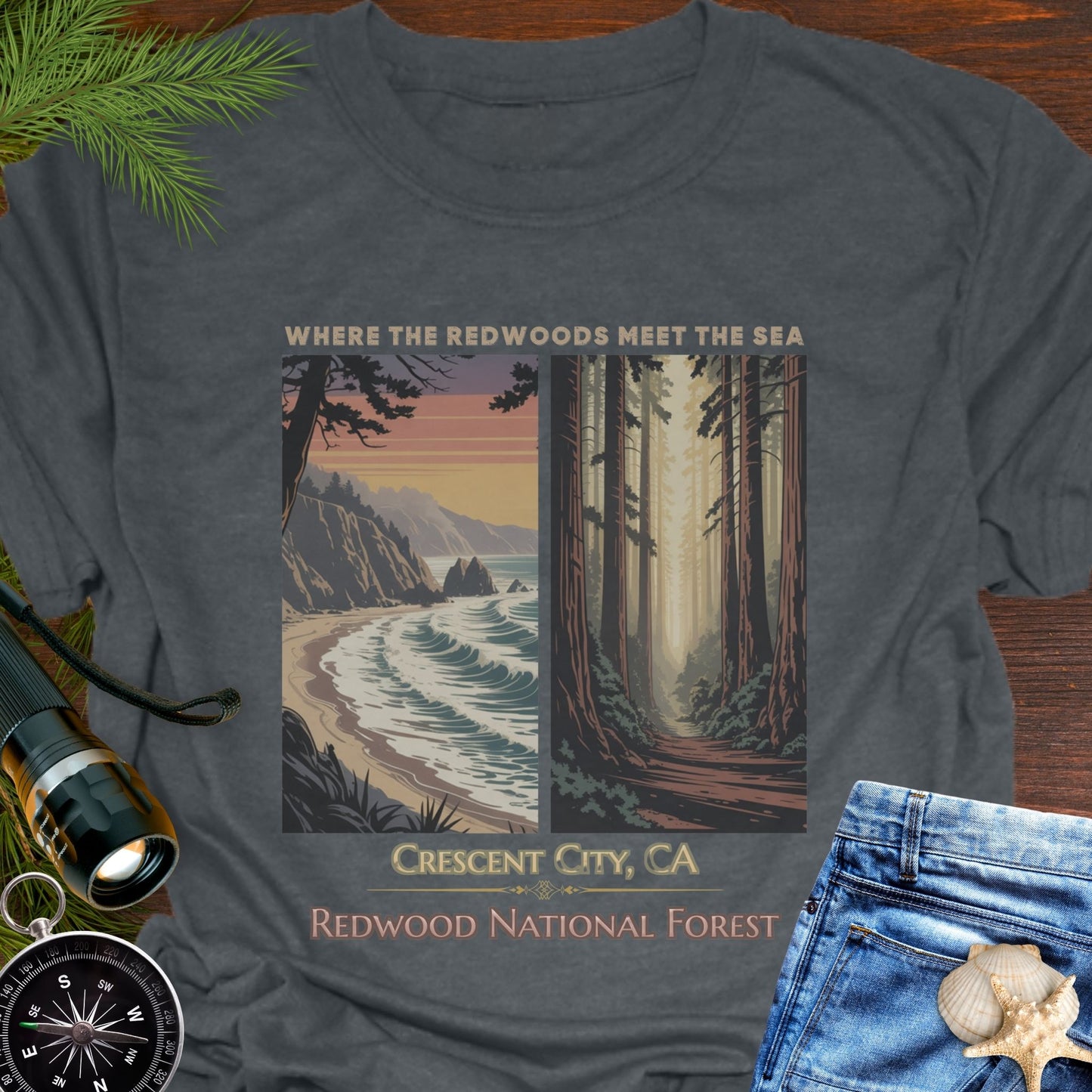 Gray t-shirt with a nature-themed design featuring Redwood National Forest, displayed on a wooden surface with outdoor accessories.
