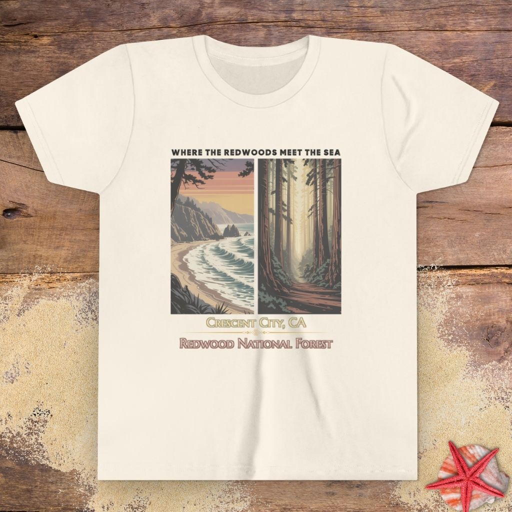 A beige short-sleeve crewneck child t-shirt featuring a graphic print of a coastal landscape and a forest, with the text 'WHERE THE REDWOODS MEET THE SEA', 'CINCUT CITY, CA', and 'REDWOOD NATIONAL FOREST'.