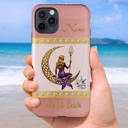 Phone case with mermaid sitting on a gold Celtic crescent moon and holding a trident with the text 'Salty Lil' Beach' on a pink and white background held by a hand on a beach background