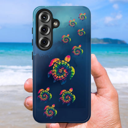 Phone case with tye dye colored turtles crawling up a marbled dark blue background design held against a beach background,