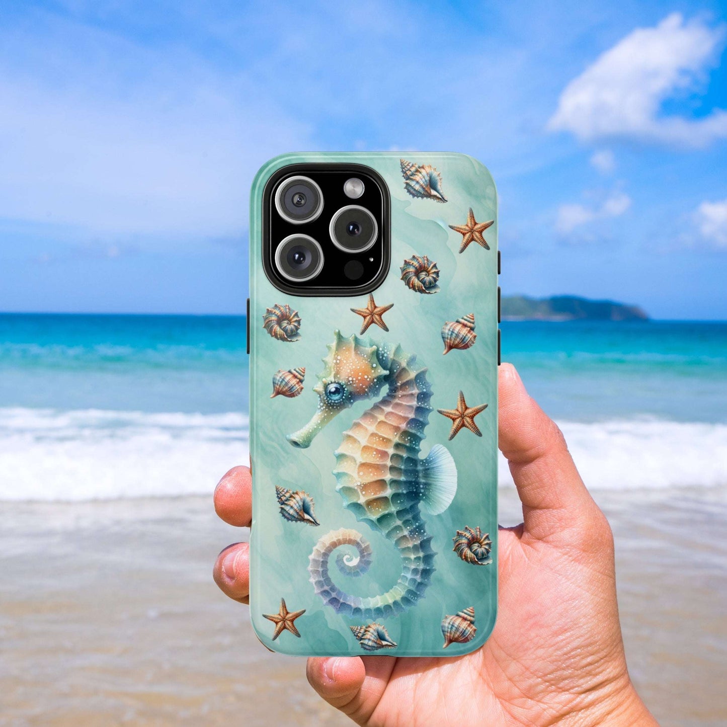 iPhone 16 Pro Max phone case with a seahorse design held in front of a beach