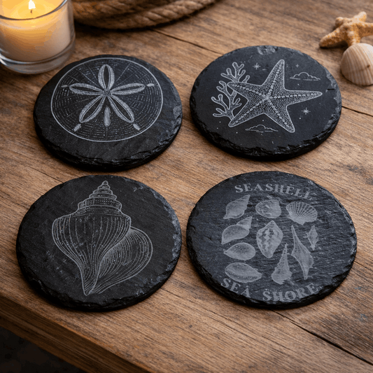 Four black slate coasters with sea-themed designs on a wooden surface.