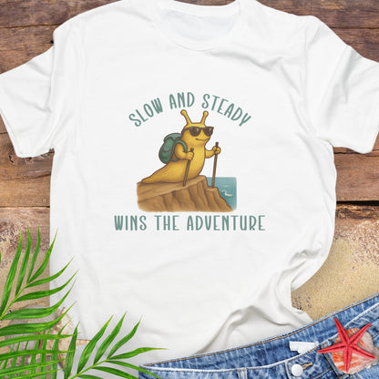 White t-shirt with a cartoon snail and text 'Slow and Steady Wins the Adventure'.