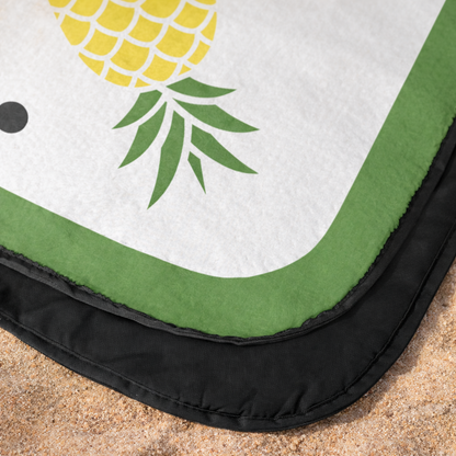 Outdoor beach blanket with pineapple design on a sandy surface