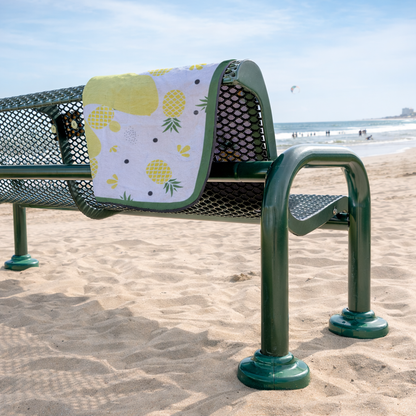 Bench with a colorful pineapple beach outdoor blanket draped over it on a sandy beach.