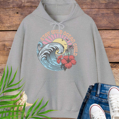 Gray hoodie with retro beach artwork featuring a stylized wave, palm trees, hibiscus flowers, and the phrase "Stay Wild Ocean Child" in sunset colors.