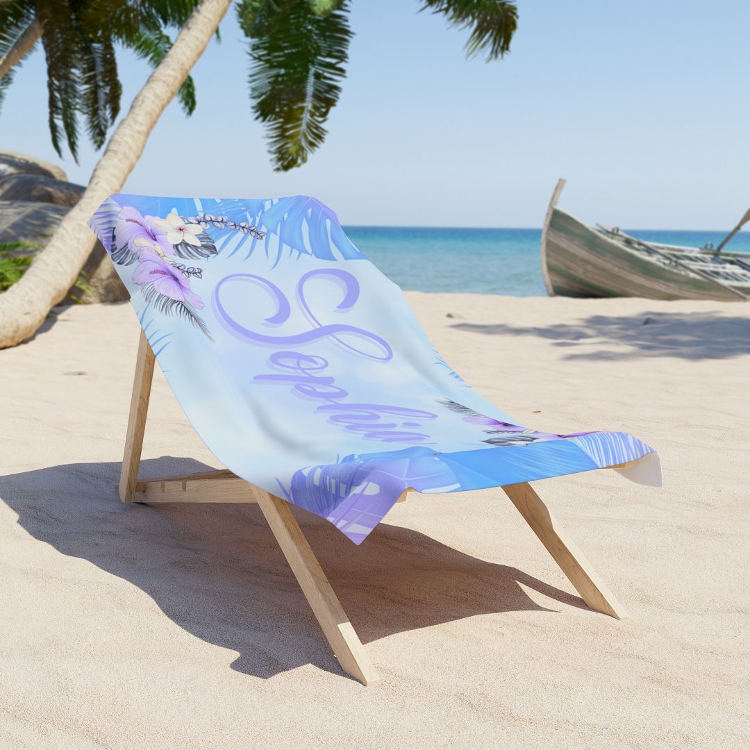 Beach towel with soft blue and purple background, hibiscus flowers and greenery in corners, and personalized name in script font.