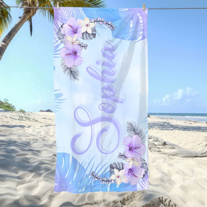 Beach towel with soft blue and purple background, hibiscus flowers and greenery in corners, and personalized name in script font.