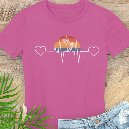 Pink t-shirt with a heart rate design featuring a sunset and palm trees on a wooden surface.