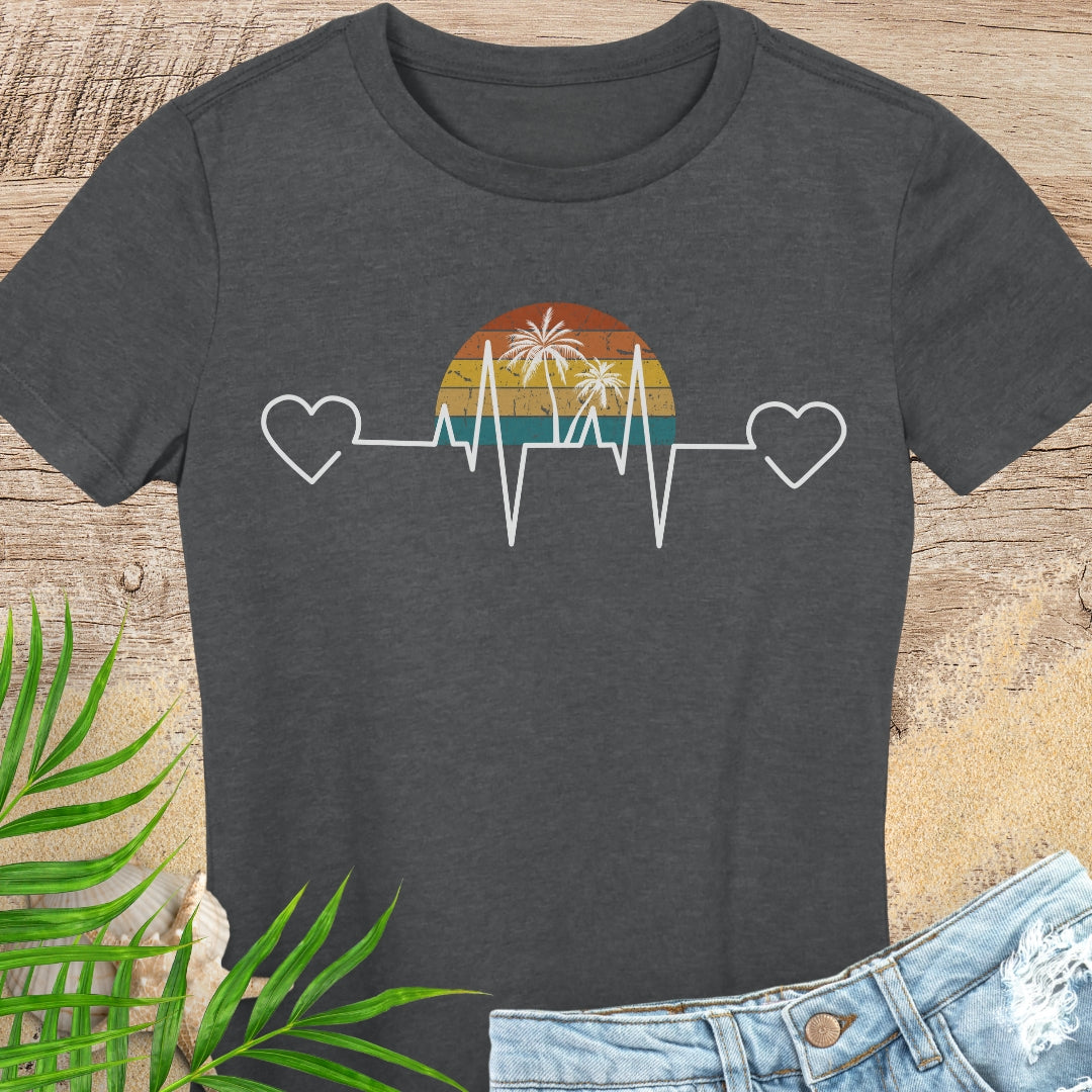Dark gray t-shirt with a heart rate design featuring a sunset and palm trees on a wooden surface.