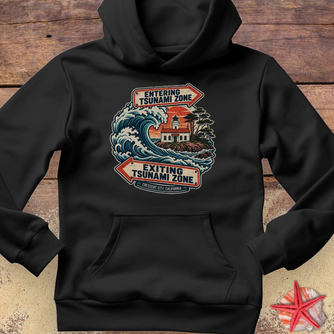 A black pullover hoodie featuring a large front graphic with a tsunami warning design in red, blue, white, and orange tones. The graphic includes directional arrows reading 'ENTERING TSUNAMI ZONE' and 'EXITING TSUNAMI ZONE' with a lighthouse and wave illustration.