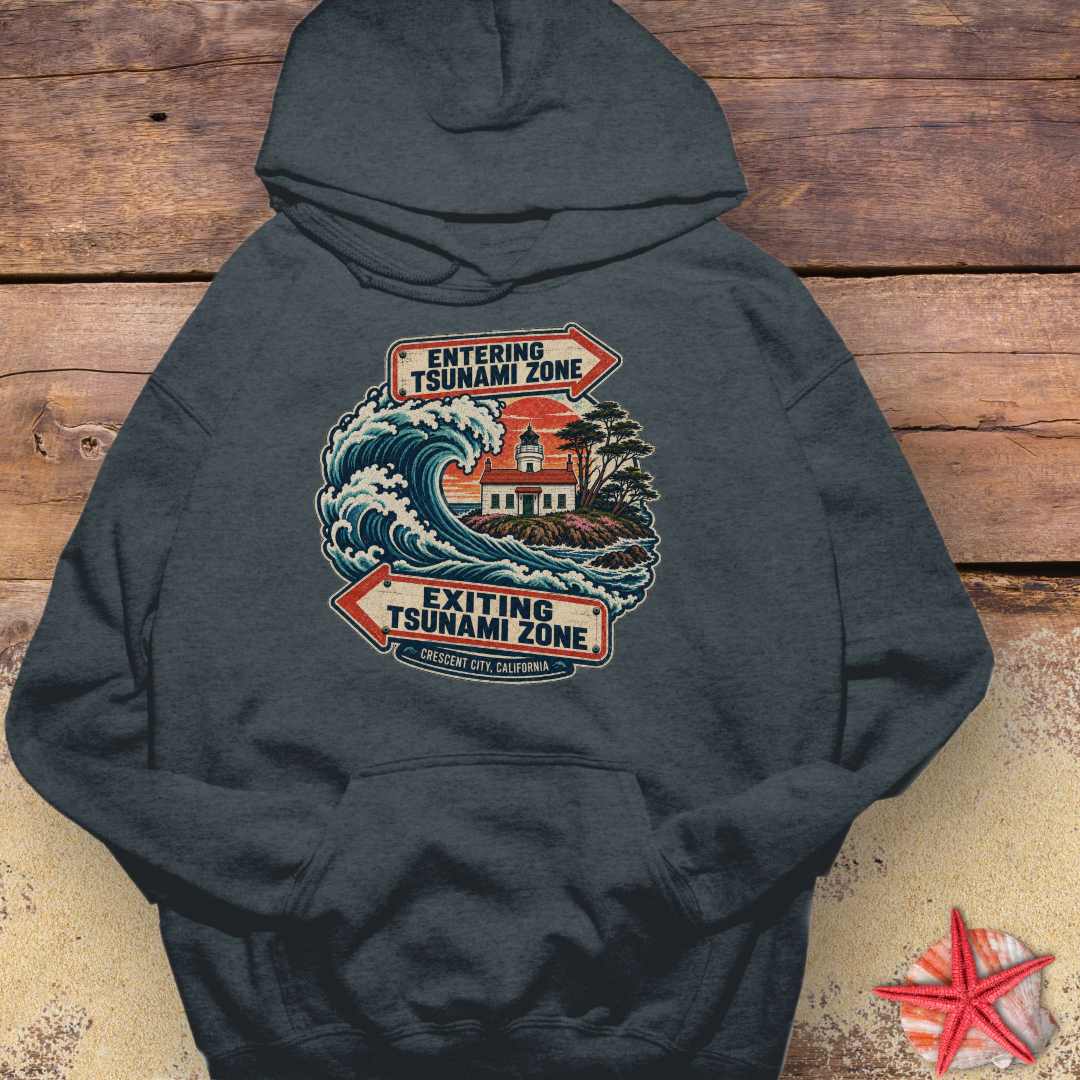 A dark charcoal gray Crescent City California hoodie design featuring a crashing ocean wave, coastal lighthouse, and vintage entering and exiting tsunami zone signs.