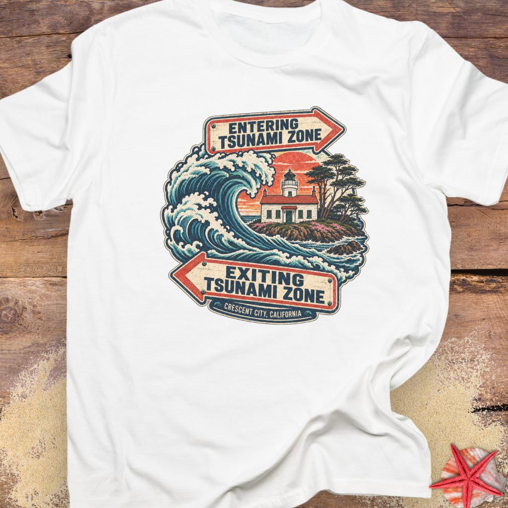 A white short-sleeve t-shirt featuring a vintage-style graphic of a tsunami wave and lighthouse with directional arrows reading 'ENTERING TSUNAMI ZONE' and 'EXITING TSUNAMI ZONE'.