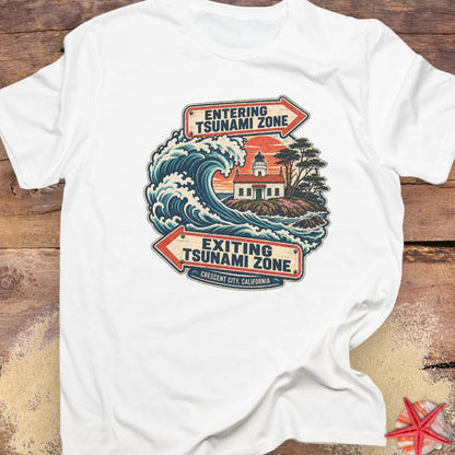 A white short-sleeve t-shirt featuring a vintage-style graphic of a tsunami wave and lighthouse with directional arrows reading 'ENTERING TSUNAMI ZONE' and 'EXITING TSUNAMI ZONE'.