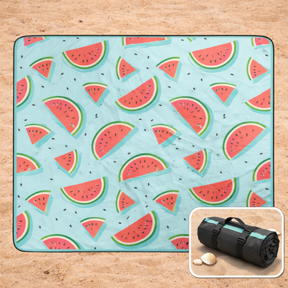 Beach blanket with watermelon pattern on a sandy beach, with it rolled-up as a tote in the corner.