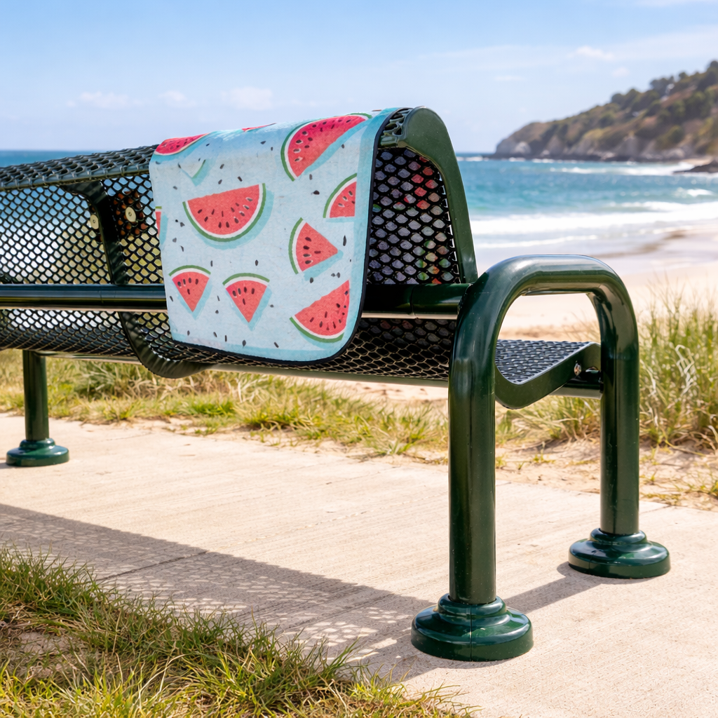 Bench with a watermelon-patterned outdoor beach blanket draped over it by the beach