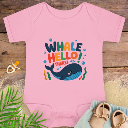 Pink baby onesie with whale design and text on a wooden surface with shoes and leaves.