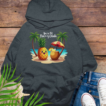 Dark gray hoodie with a pineapple and a coconut pina colada on a beach between two palm trees with the text You're the Pina to my Colada.